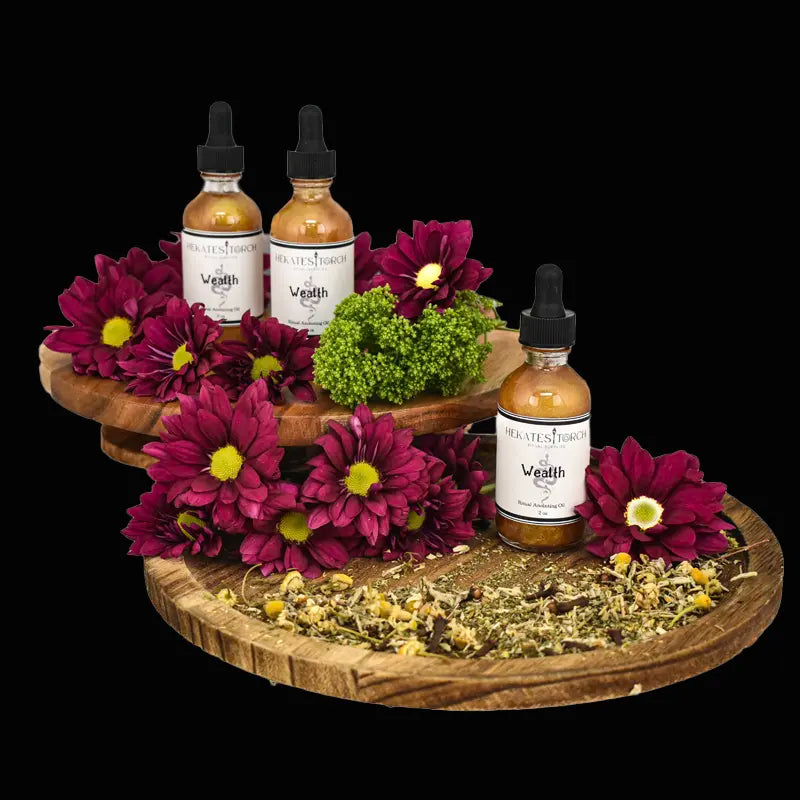 Hekate's Wealth Oils on a wooden tray surrounded by flowers and herbs